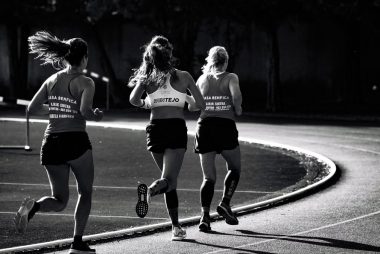 Black and white back view of unrecognizable fit female runners in sportswear running during track and field competition